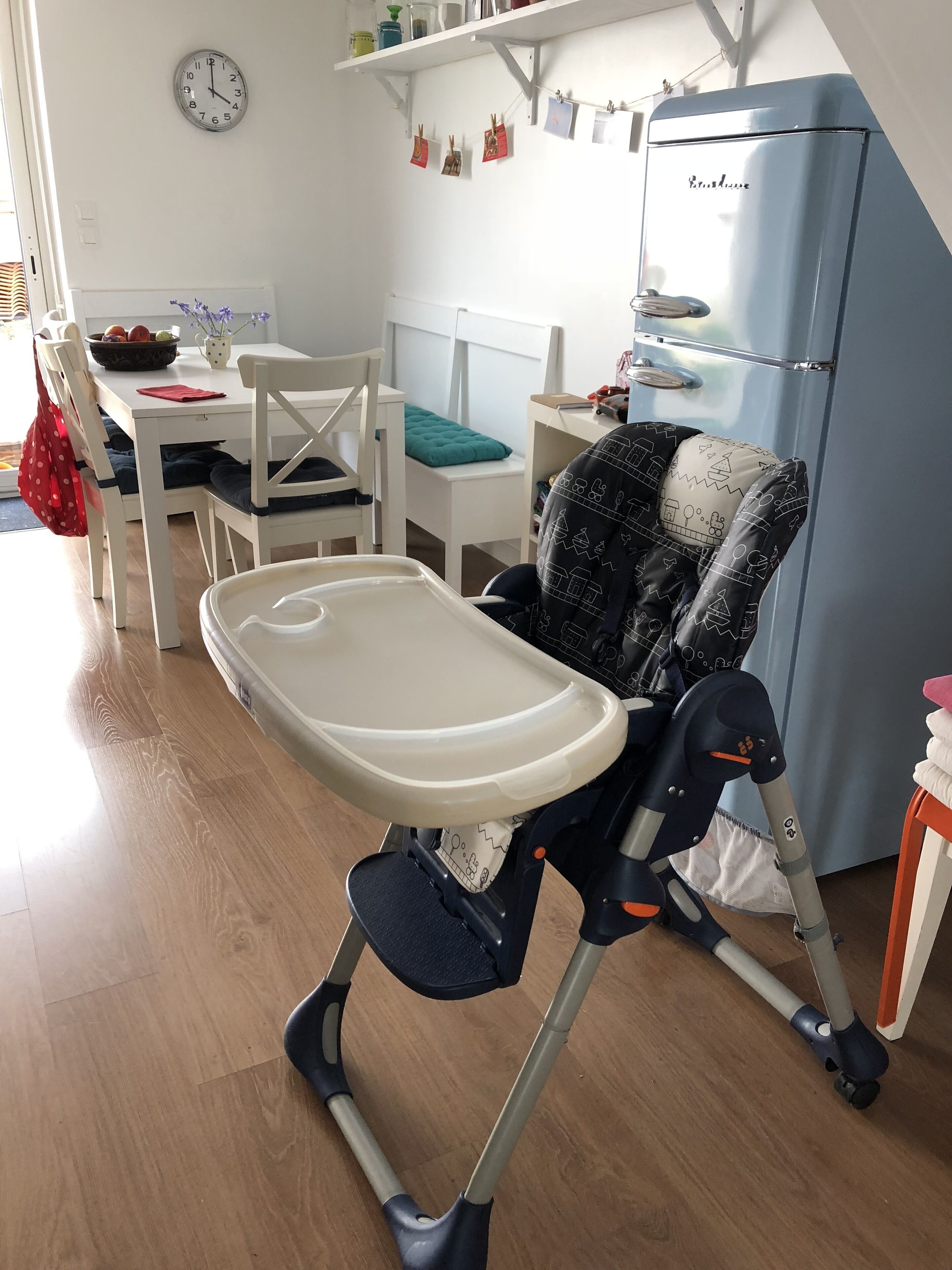 A modern kitchen with a white refrigerator, a dining table with chairs, and a baby high chair.