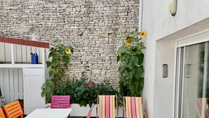 Een terras buiten met een witte tafel en oranje stoelen, een stenen muur en potplanten.
