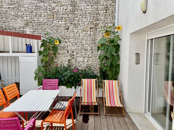 An outdoor patio with a white table and orange chairs, a stone wall, and potted plants.