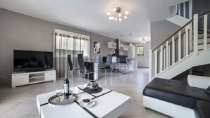 Una sala de estar moderna con televisor de pantalla plana, un comedor con una cocina al fondo y una escalera que sube.