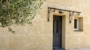 Un edificio con fachada beige texturizada, una puerta oscura y un ventanal pequeño con una lámpara encima.