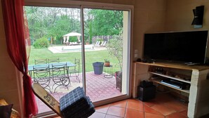 A room with a sliding glass door leading to a backyard with a patio, outdoor furniture, and a TV on a stand.
