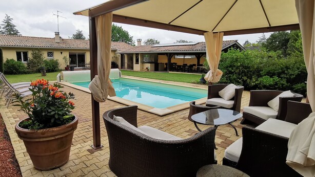 A covered outdoor seating area with wicker furniture and a pool in the background.