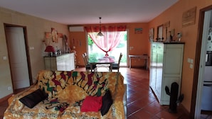 A living room with a sofa, a dining table, and a kitchen area with a refrigerator.