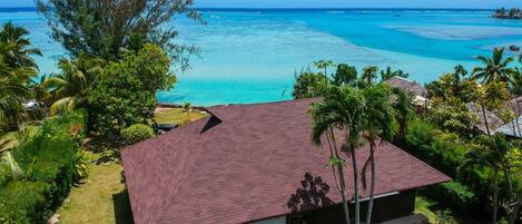 A house with a red roof, surrounded by lush greenery and a view of the turquoise ocean.
