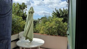A patio with a white table and a green umbrella, surrounded by greenery and a clear sky. - GROUND FLOOR DIRECT ACCESS BEACH 'uncrowded' Gde Terrace (Le Barcarès)