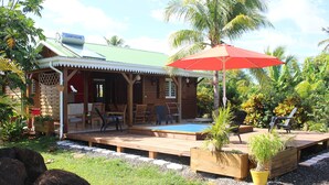 A wooden house with a pool, outdoor seating, and a red umbrella.