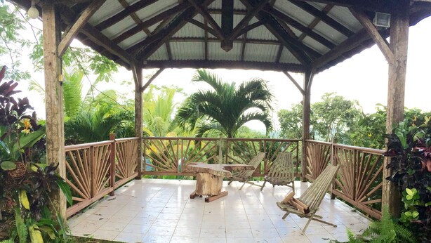 A wooden gazebo with a tiled floor, surrounded by lush tropical plants.