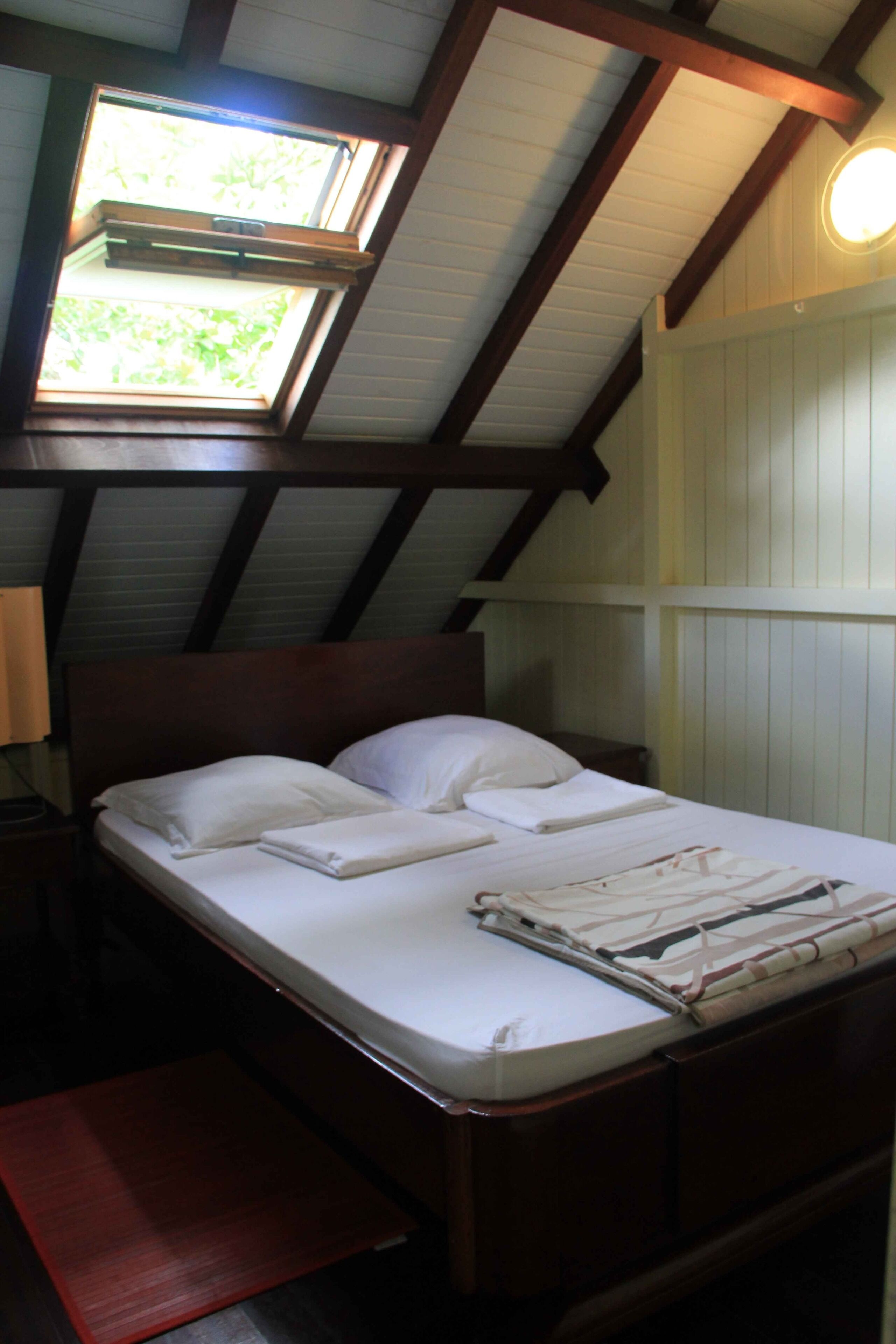 Un dormitorio con una cama de madera, un tragaluz y una mesita de noche con lámpara.