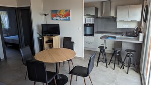 Una cocina moderna con comedor, que incluye una mesa redonda de madera, sillas negras y un televisor sobre un mueble.