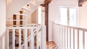 A staircase with white railings and wooden beams, leading to a door with a view of trees outside.
