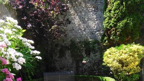 A patio with a table and chairs, surrounded by well-maintained hedges and flowering plants.