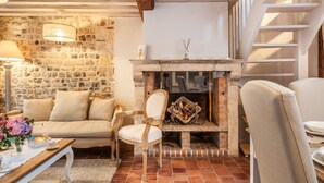 A cozy living room with a stone wall, a fireplace, and a wooden ceiling.