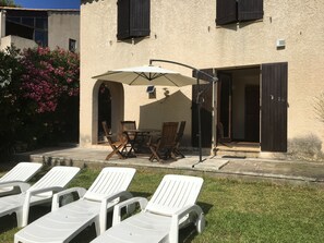 A patio with a table and chairs, a covered area with an umbrella, and white lounge chairs. - Beautiful Studio in a large Provencal Villa - Swimming pool (Sausset-Les-Pins)