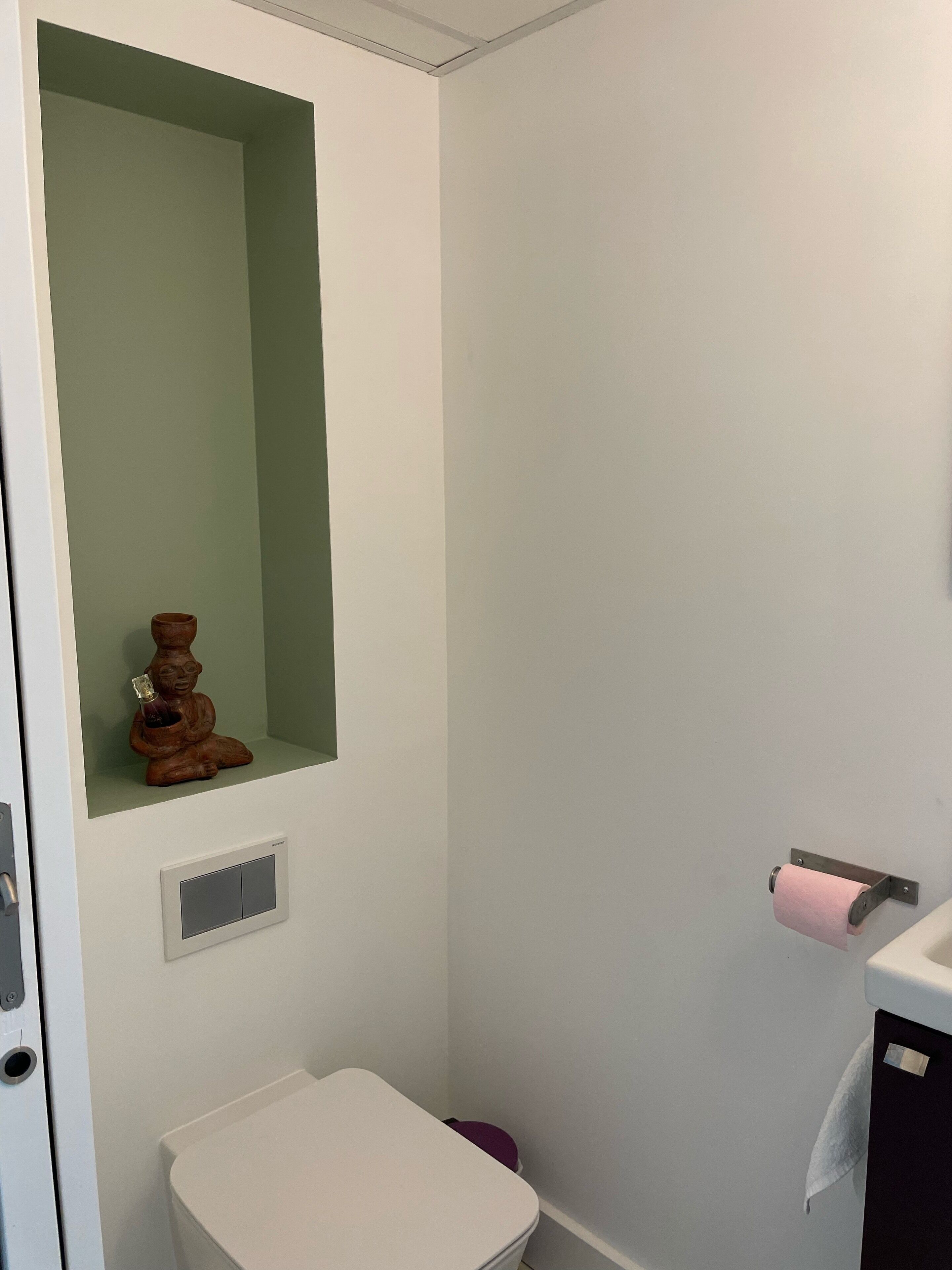 A small bathroom with a toilet, a shelf with a decorative item, a towel rack, and a vent.
