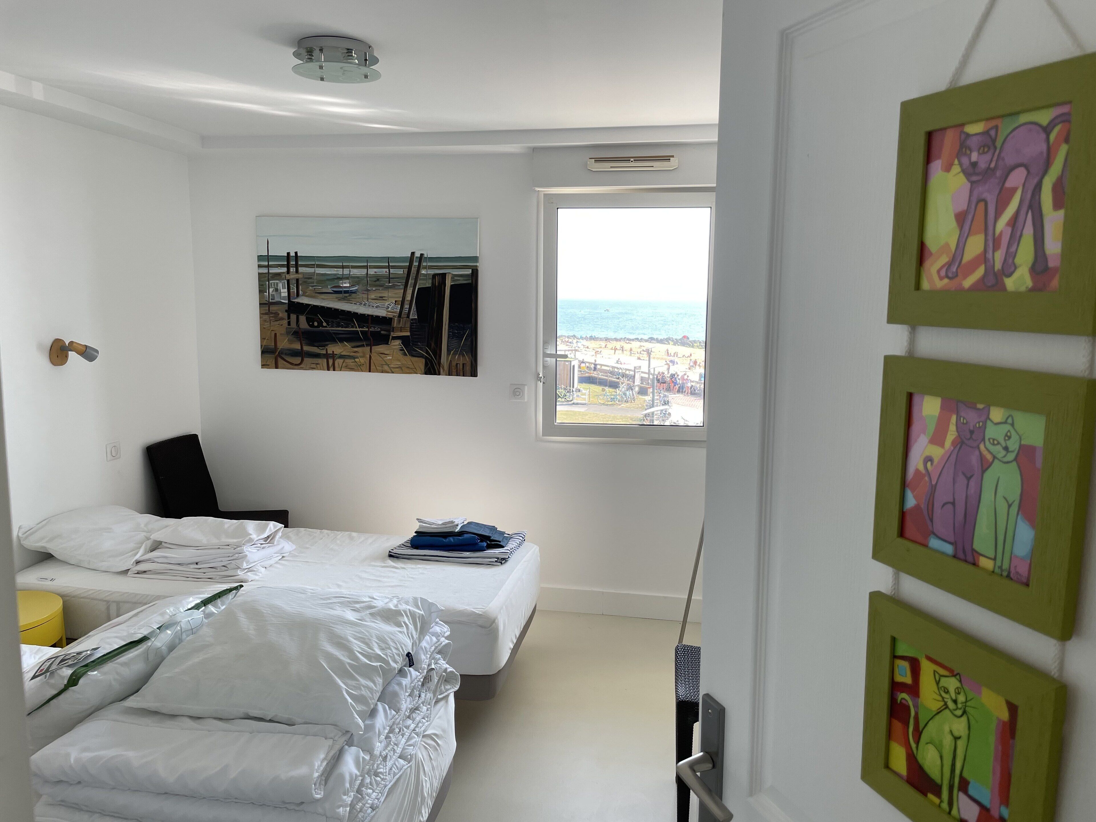 Une chambre avec deux lits, une fenêtre donnant sur la plage et des œuvres d’art accrochées au mur.