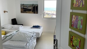 Een slaapkamer met twee bedden, een raam met uitzicht op het strand en kunst aan de muur.