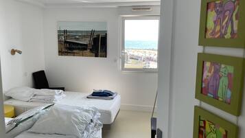 Une chambre avec deux lits, une fenêtre donnant sur la plage et des œuvres d’art accrochées au mur.