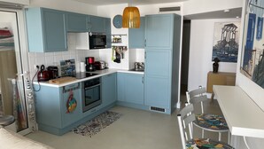 Een moderne keuken met blauwe kastjes, een magnetron, een koffiezetapparaat, en een eethoek met een witte tafel en kleurrijke stoelen.