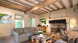 Ein gemütliches Wohnzimmer mit Holzbalkendecke, Kamin, einer Couch, einem Couchtisch und einem Bücherregal.