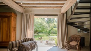 Ein Zimmer mit Blick auf einen Garten, ein Holzschrank, ein Korbstuhl und ein Sofa mit Decke.