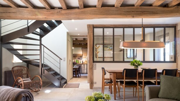 Ein modernes Wohnzimmer mit Treppe, Holzbalken, Essbereich und großem Fenster.