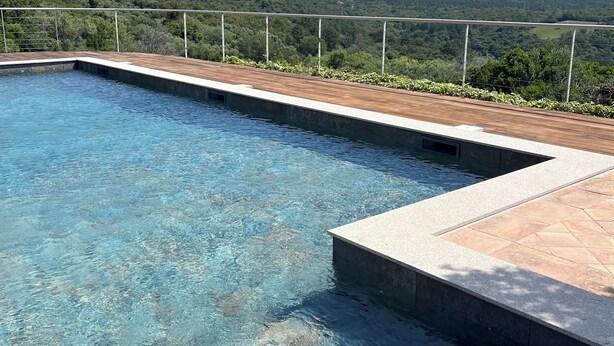 A clear swimming pool with a wooden deck and a metal railing, surrounded by lush greenery and mountains in the background. - Apartment in renovated pool villa 2025 (Porto-Vecchio)