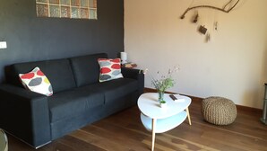A modern living room with a black sofa, a small white table, and a decorative wall piece. - Apartment in renovated pool villa 2025 (Porto-Vecchio)