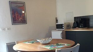 A dining area with a wooden table, two chairs, a bowl, and a framed picture on the wall. - Apartment in renovated pool villa 2025 (Porto-Vecchio)