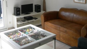 A living room with a brown leather sofa, a white entertainment unit with speakers, a glass display case with various items, and several framed artworks on the wall. - MODERN HOUSE CROZON MORGAT (Crozon)