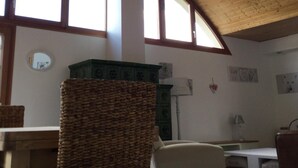 Une pièce avec un haut plafond en bois, de grandes fenêtres, un fauteuil en osier, une chaise blanche et une petite table.