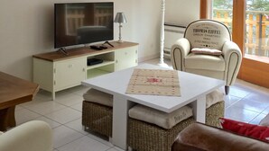 Un salon avec un téléviseur, une lampe, un fauteuil et une table.
