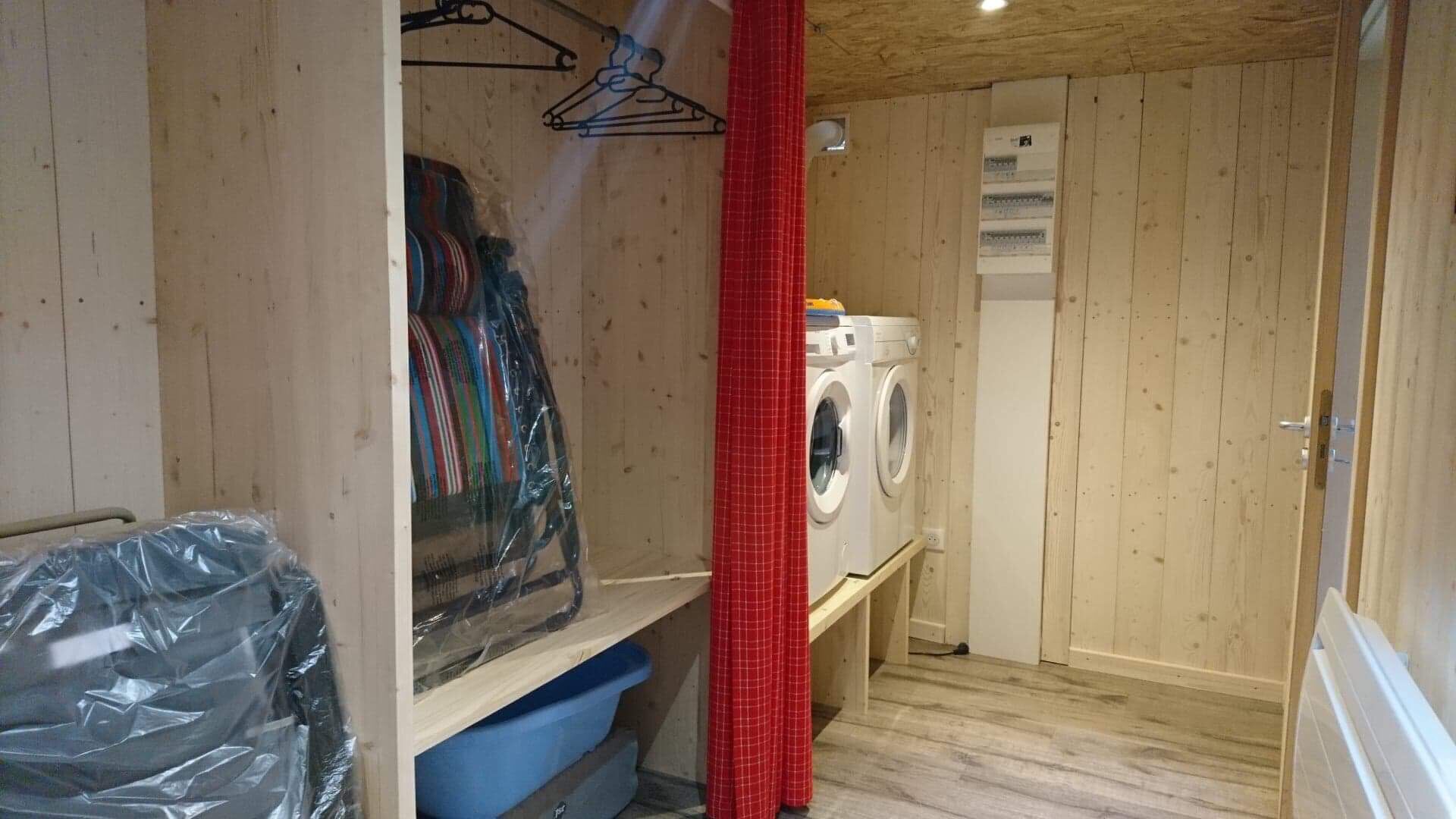 A small laundry room with a washing machine, a drying rack, and a blue storage bin.
