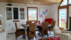Un coin repas avec des chaises en osier, une table en bois et un buffet blanc aux portes vitrées.