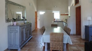 Un vaste espace dédié à la salle à manger, avec une longue table, des chaises en osier et un buffet agrémenté d’un miroir.