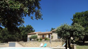 Une maison avec un mur en pierre, une piscine et deux chaises longues.