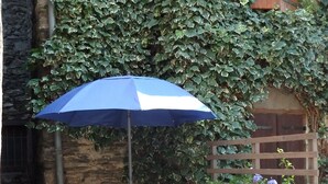 Two lounge chairs with a blue umbrella, a wooden planter with flowers, and a stone wall. - Spacious barn, comfortable for family stay. Charming place, outdoor terrace (Bagnères-de-Luchon)