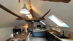 A dining area with a wooden table and chairs, a kitchen with black cabinets and a countertop, and a sloped ceiling with exposed beams. - Spacious barn, comfortable for family stay. Charming place, outdoor terrace (Bagnères-de-Luchon)