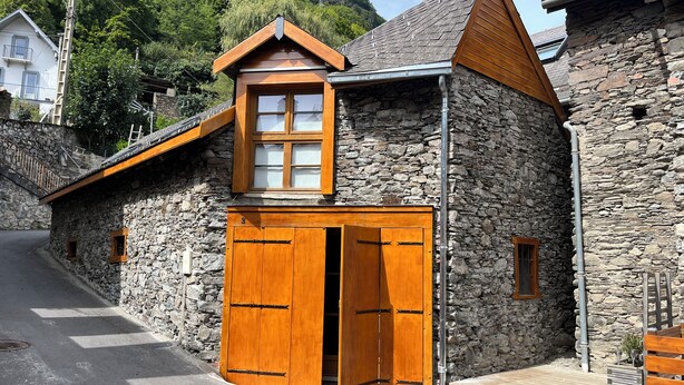 A stone building with a wooden door and window, a staircase, and a view of a mountain. - Spacious barn, comfortable for family stay. Charming place, outdoor terrace (Bagnères-de-Luchon)