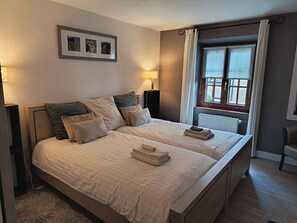 Un lit bien fait, avec des oreillers, une table de chevet avec une lampe, une fenêtre avec des rideaux et un tableau encadré au mur.