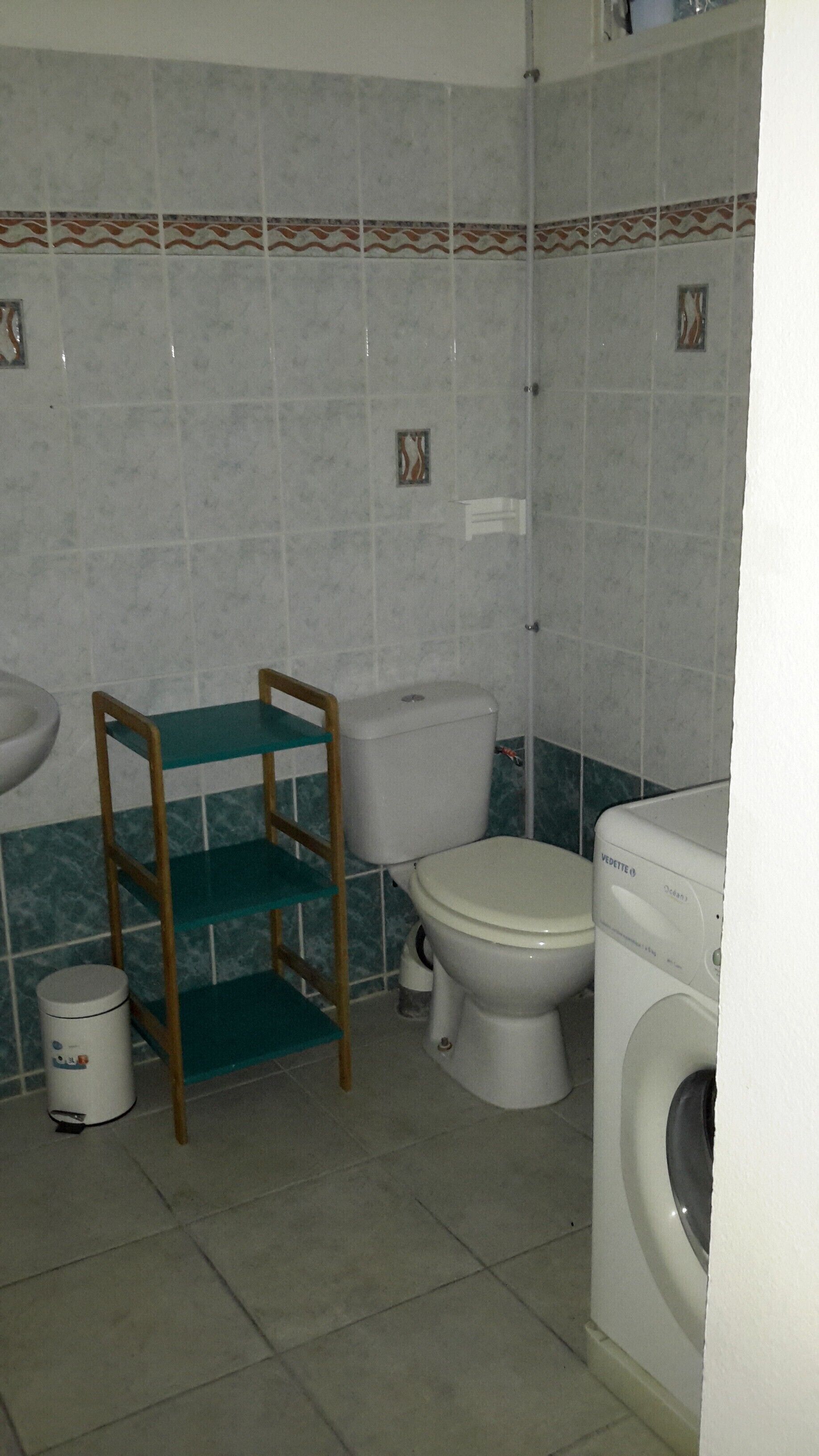 Une petite salle de bain comprenant des toilettes, un lave-linge et une chaise en bois avec un siège vert.