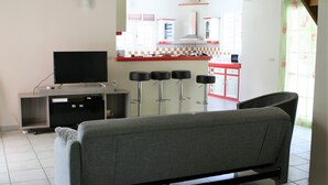Un salon comprenant un canapé, un téléviseur et un coin cuisine avec des tabourets de bar.