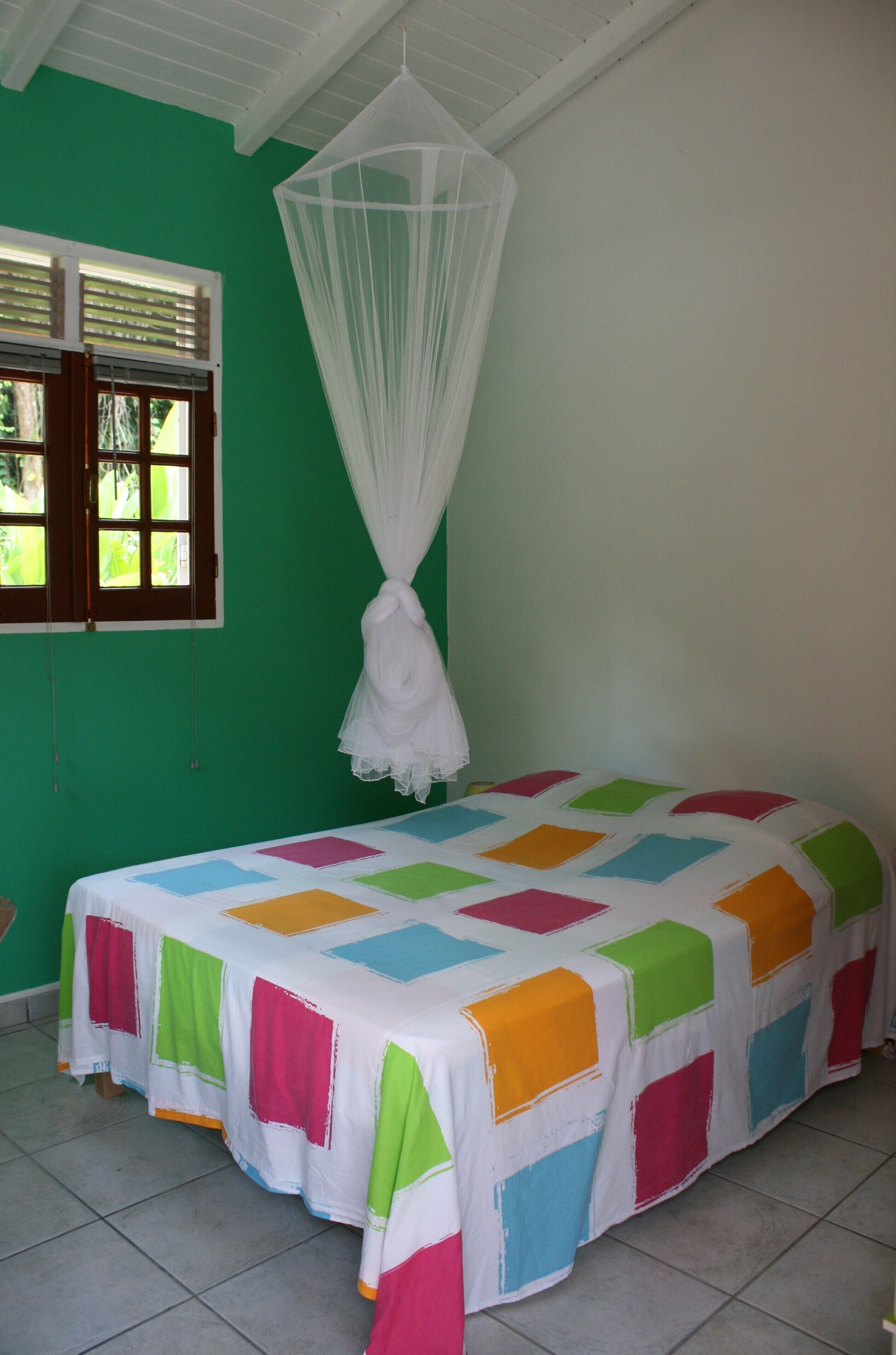 A room with a bed covered in a colorful quilt, a white canopy, and a window with blinds.