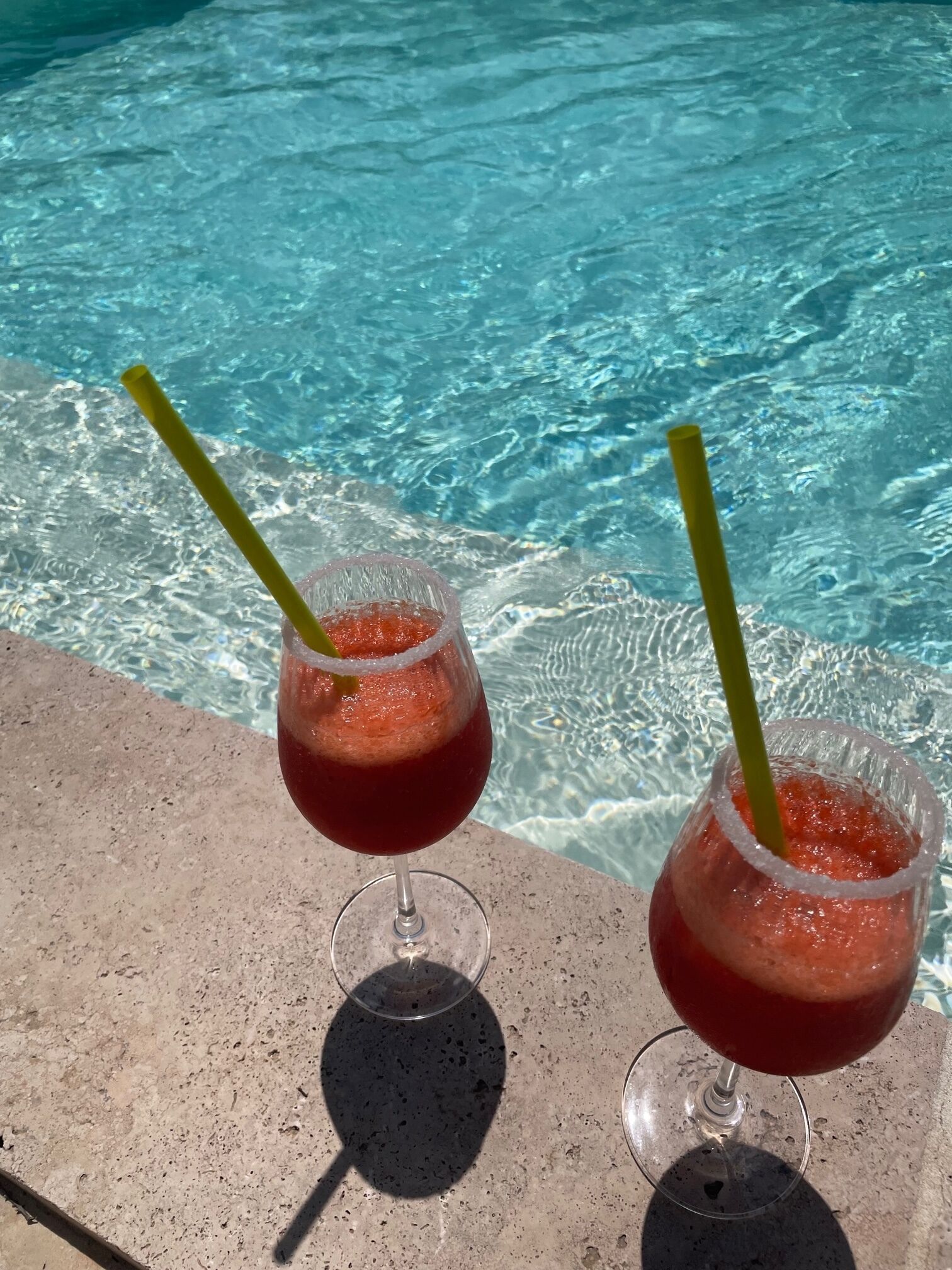 Two glasses of red drink with straws by a poolside.