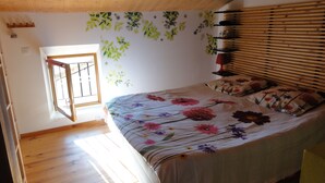 Ein Schlafzimmer mit Holzboden, einer Holzbalkendecke, einem Bett mit Blumenmuster-Bettwäsche und einem Fenster mit Jalousien.