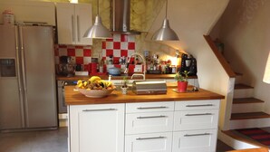 Eine Küche mit einer zentralen Kochinsel, weißen Schränken, einem Edelstahl-Kühlschrank und einer karierten Spritzschutzwand.
