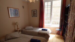 Habitación de hotel con dos camas, una mesita con lámpara, una ventana con cortinas y vistas al exterior.