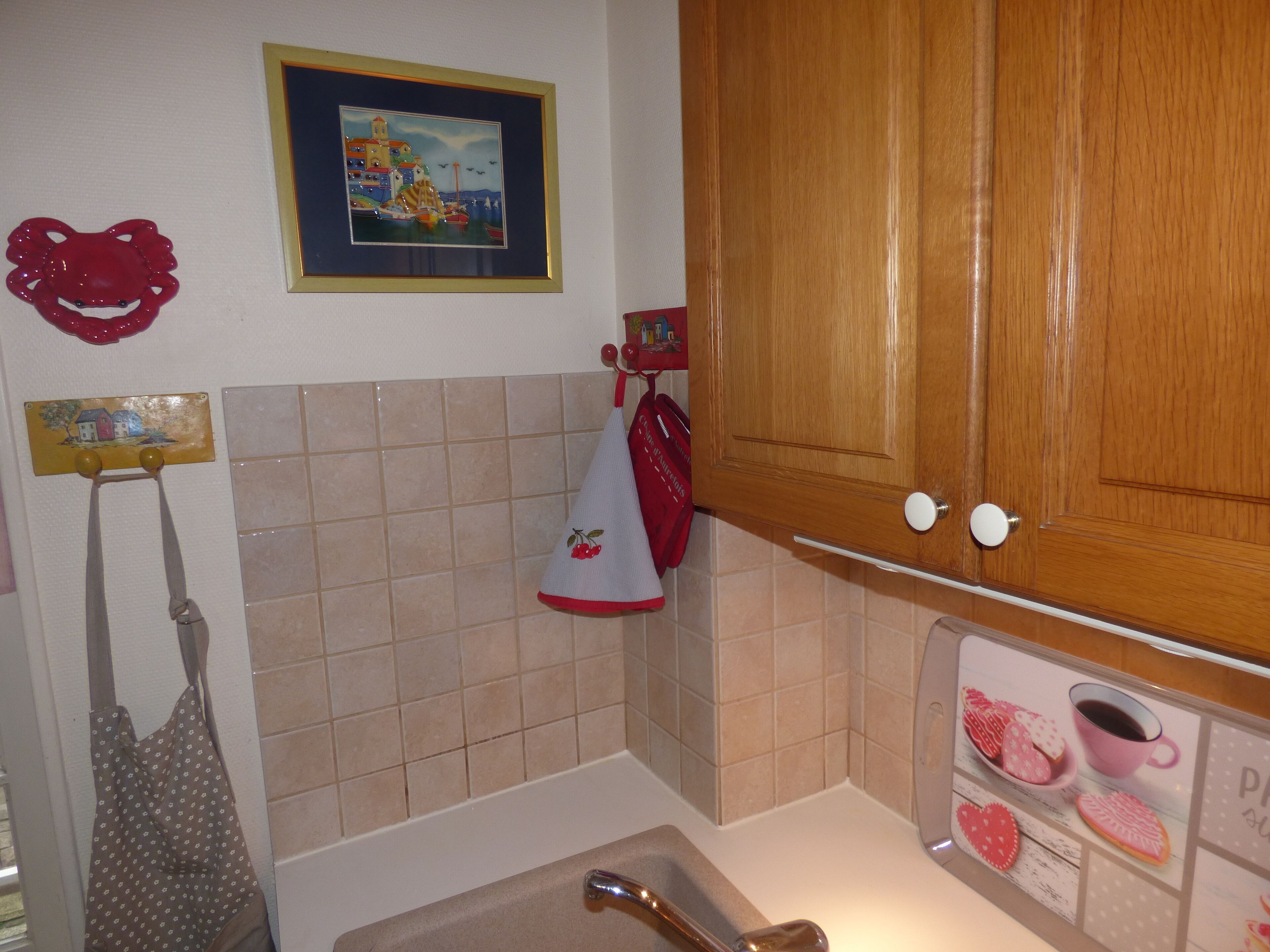 Une cuisine avec des meubles de rangement en bois, un pare-feu en carrelage, un tableau encadré et un tablier décoratif accroché au mur.