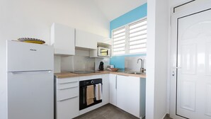 Una cocina compacta con armarios blancos, horno integrado, microondas y fregadero.
