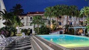 A swimming pool with lounge chairs, surrounded by palm trees and a building with a red roof.